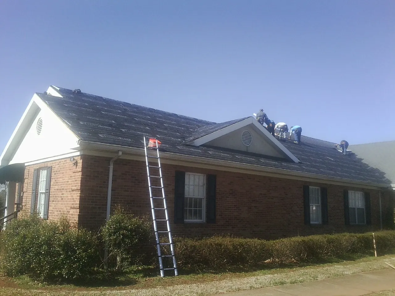 Crew tearing shingles off a brick ranch roof with a ladder set — Emergency Roof Repair work by our crew in Fleming