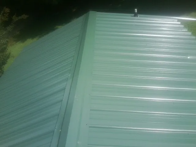 New green metal panels meeting at the ridge of a roof — Flat Roof Repair work by our crew in Fleming